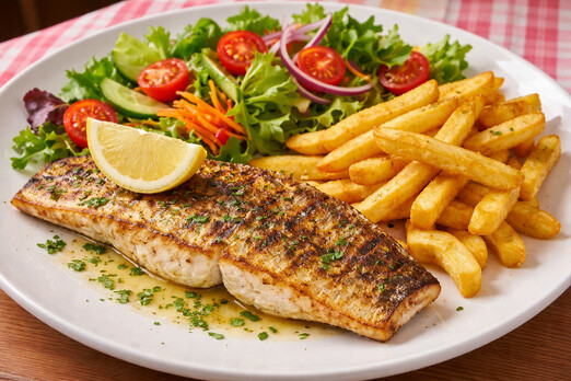 Gegrilltes Zanderfilet mit Pommes, Zitronenscheibe und frischem Salat auf einem Teller angerichtet